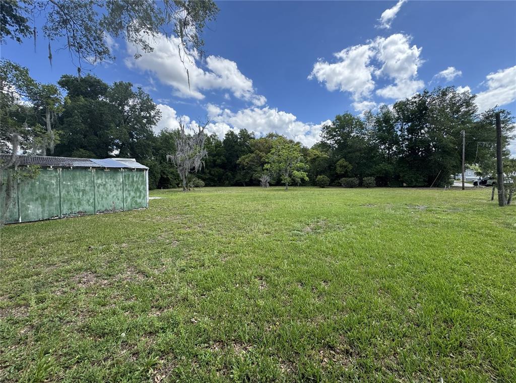 A large, grassy vacant lot features a green storage shed and mature trees — 65 HOWARD STREET, UMATILLA, FL