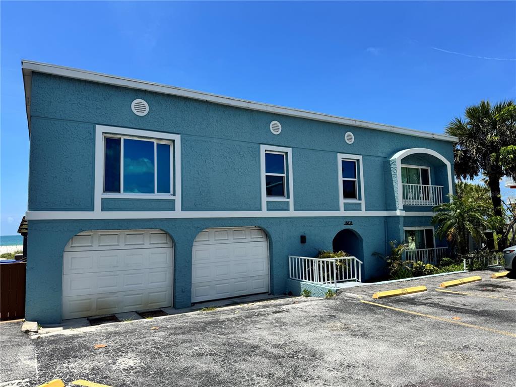 A two-story blue building with two garage doors, white trim, and an arched balcony — 18838 GULF BOULEVARD UNIT 202, INDIAN SHORES, FL