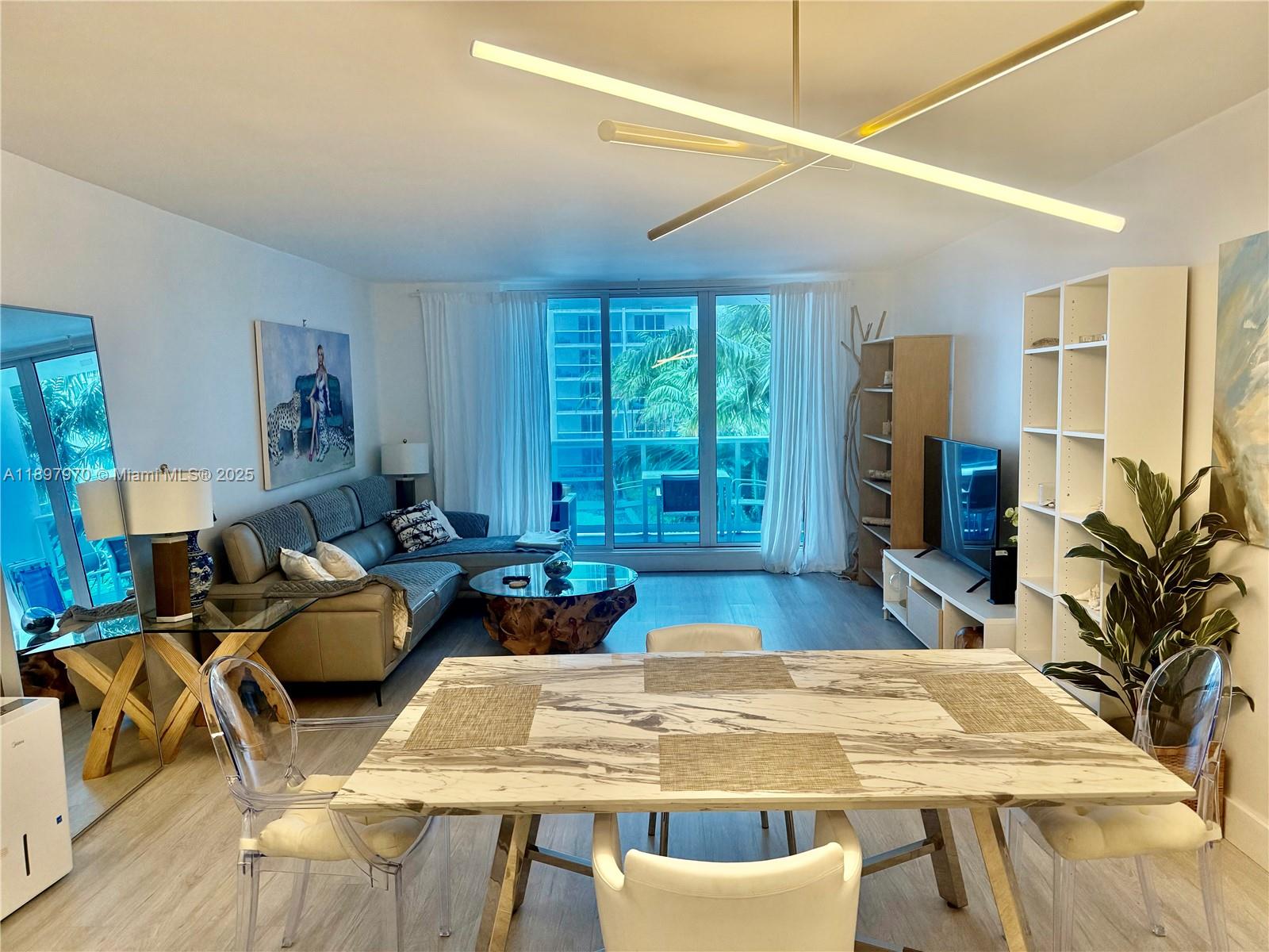 A living and dining area features a marble table, modern lighting, and a balcony view — 2301 Collins Ave # 619, Miami Beach FL 33139, MIAMI BEACH, FL