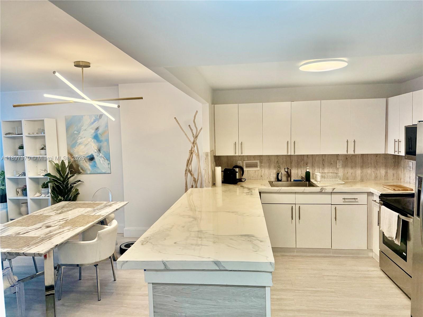 A modern kitchen features white cabinetry, marble-patterned countertops, and an adjacent dining area — 2301 Collins Ave # 619, Miami Beach FL 33139, MIAMI BEACH, FL