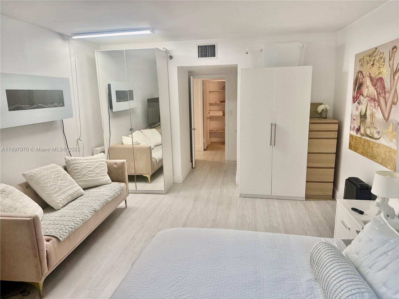 A bedroom features a pink sofa, a mirrored wardrobe, a white cabinet, and light wood flooring — 2301 Collins Ave # 619, Miami Beach FL 33139, MIAMI BEACH, FL