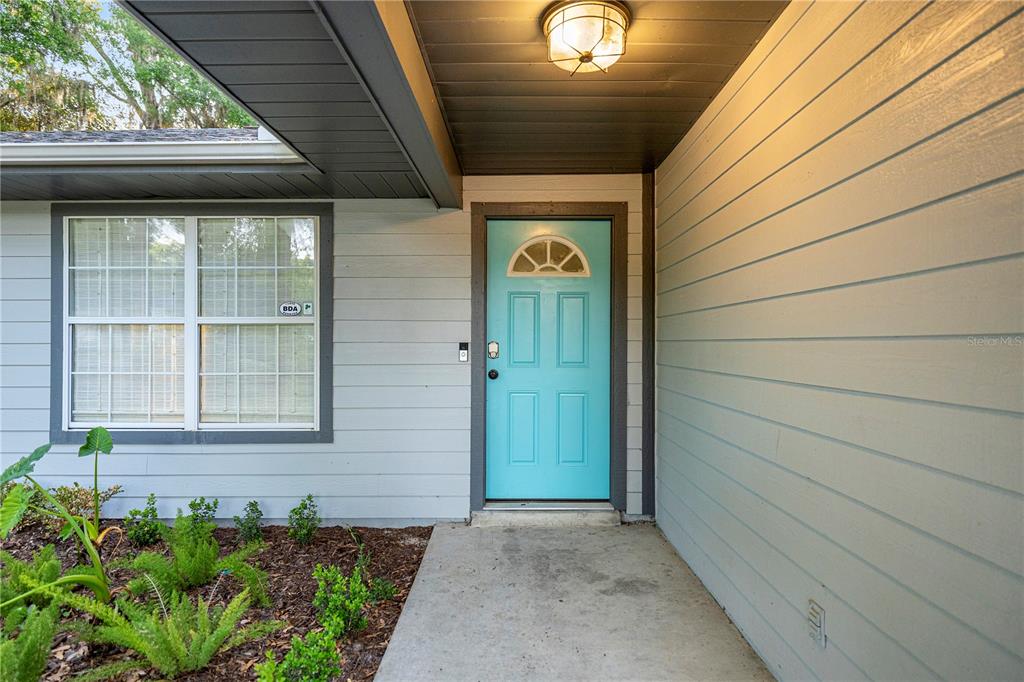 A light blue front door with a window sits under a covered porch entrance — 6525 NW 62ND AVENUE, OCALA, FL