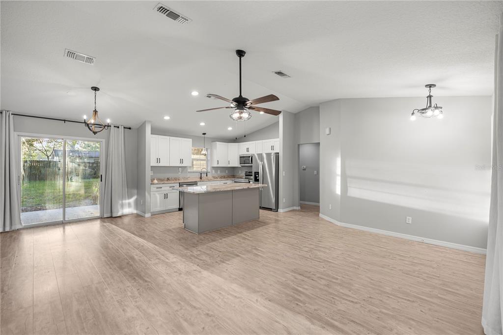 An open-concept kitchen and living area features light wood flooring, white cabinets, and a central island — 6525 NW 62ND AVENUE, OCALA, FL
