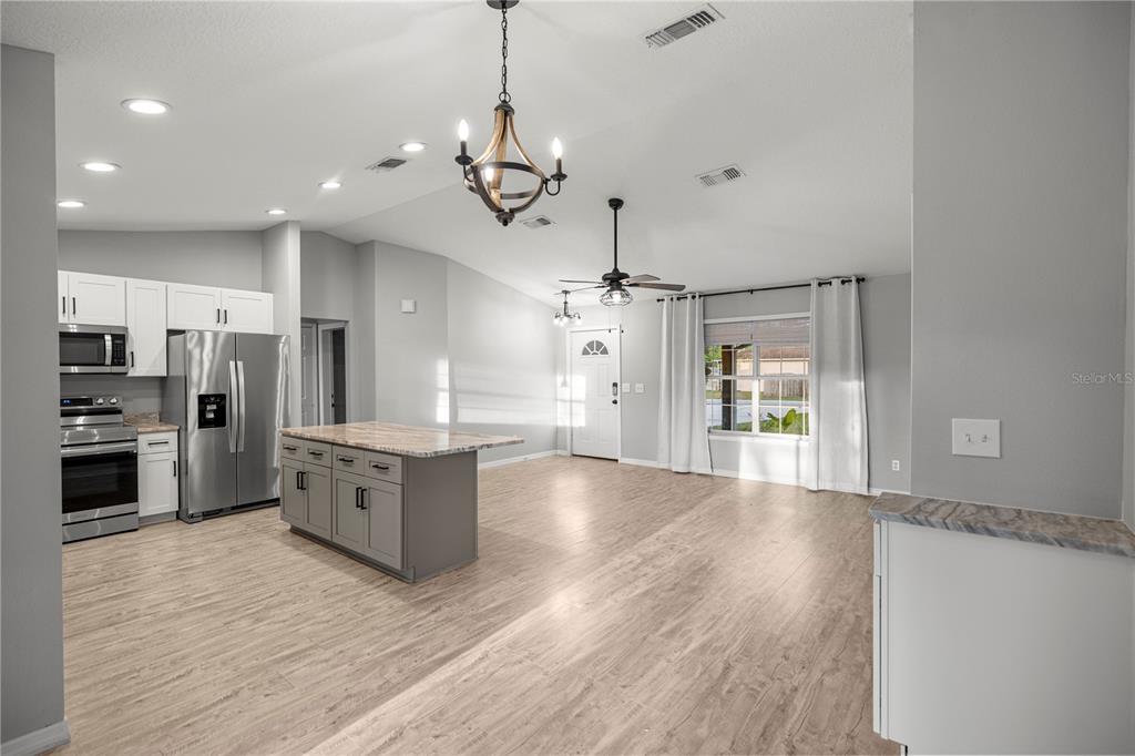 A kitchen with a gray island and stainless steel appliances opens into a living area — 6525 NW 62ND AVENUE, OCALA, FL