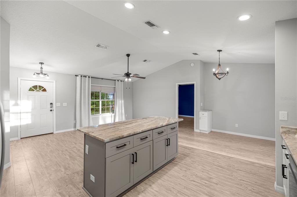 A kitchen island with gray cabinets and a stone countertop sits in an open-concept room — 6525 NW 62ND AVENUE, OCALA, FL