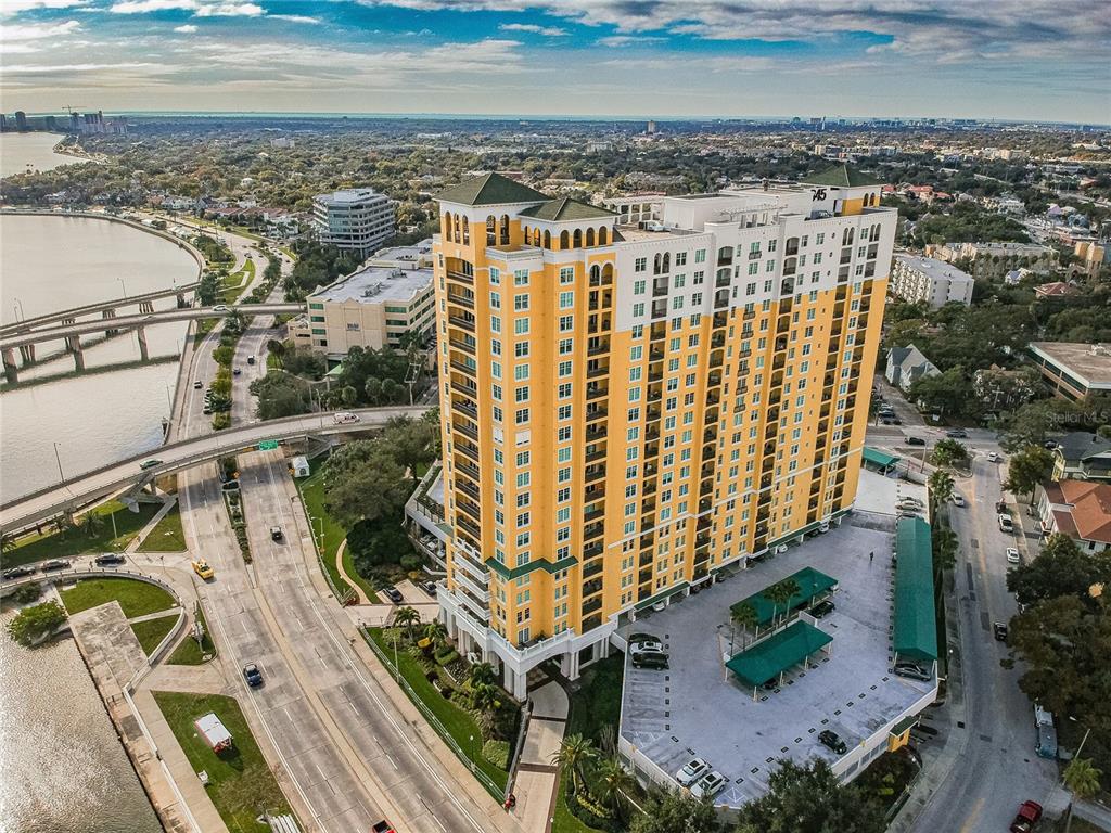 An aerial view shows a tall, yellow multi-story residential building located near a bridge and water — 345 BAYSHORE BOULEVARD UNIT 1710, TAMPA, FL