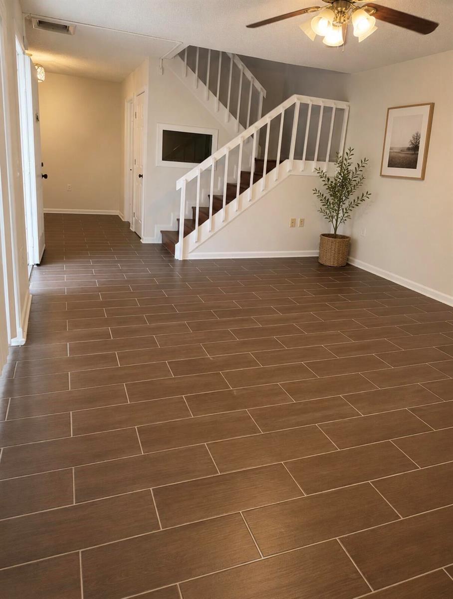 An entryway with brown wood-look tile flooring, a white staircase, and a potted plant — 1421 14th Lane # D, FL 33463, FL