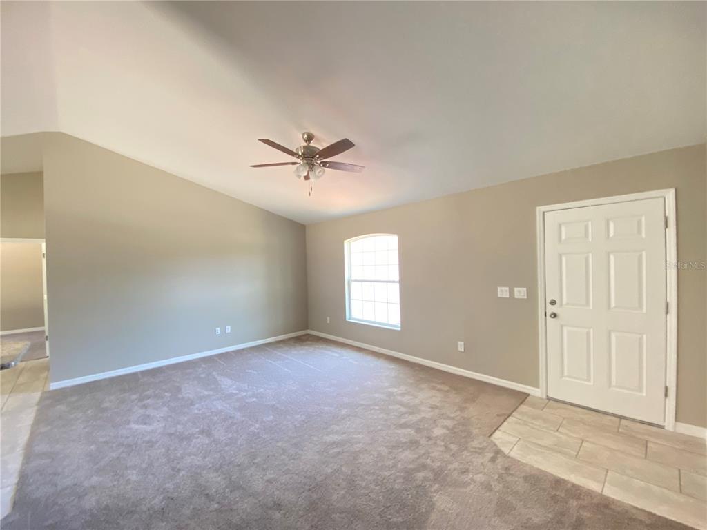 An empty living room features beige walls, carpeted flooring, a ceiling fan, and a front door — 4217 SW 162ND PLACE, OCALA, FL