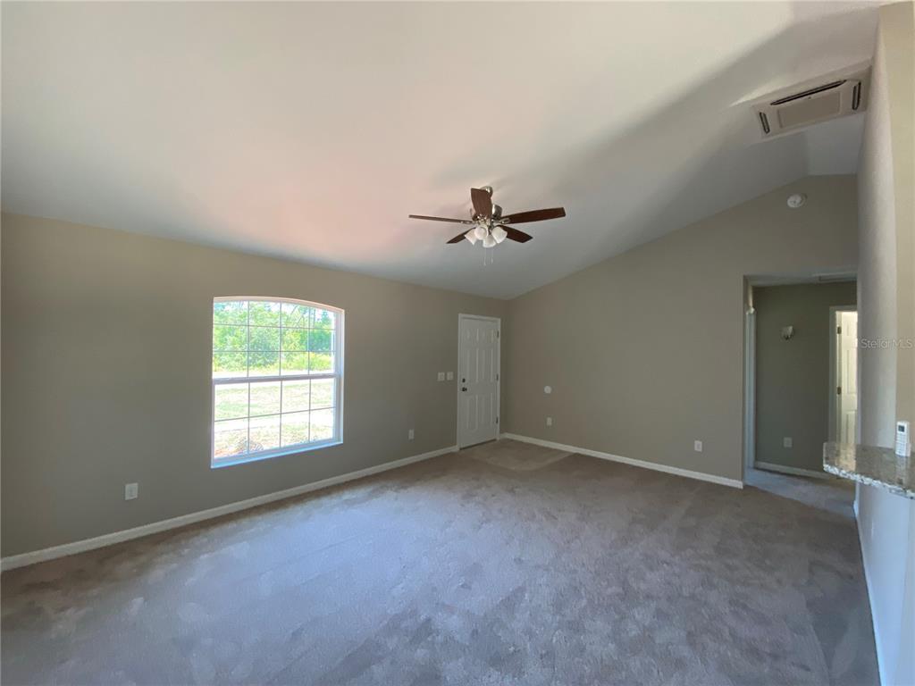 An empty room with beige walls, carpeted flooring, a vaulted ceiling, and a ceiling fan — 4217 SW 162ND PLACE, OCALA, FL