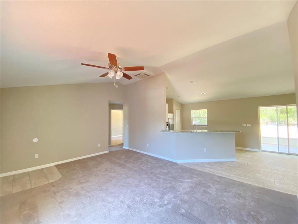 A living room with carpeted flooring transitions to a tiled kitchen area with a breakfast bar — 4217 SW 162ND PLACE, OCALA, FL