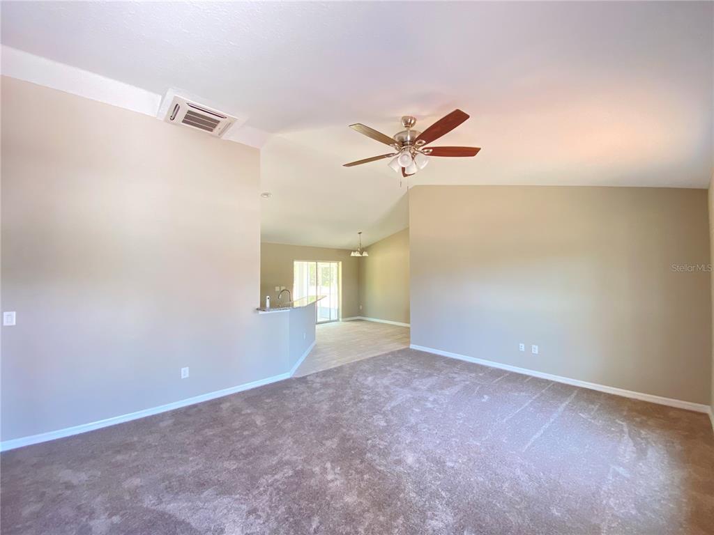 A living room with beige carpet, vaulted ceilings, a ceiling fan, and a kitchen pass-through — 4217 SW 162ND PLACE, OCALA, FL