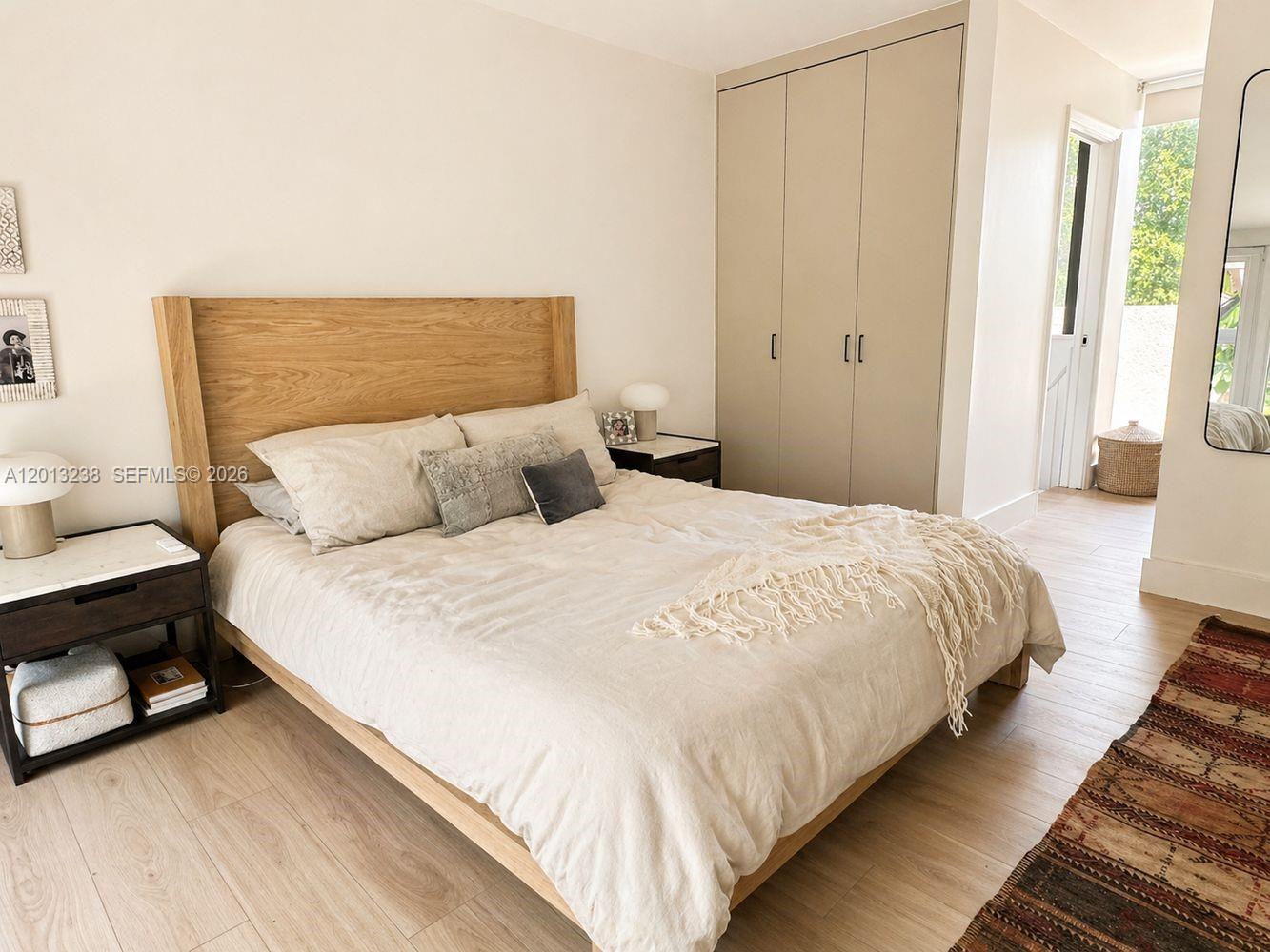 A bedroom features a wooden bed frame, beige bedding, built-in closets, and light wood flooring — 2984 Mary St, Miami FL 33133, MIAMI, FL