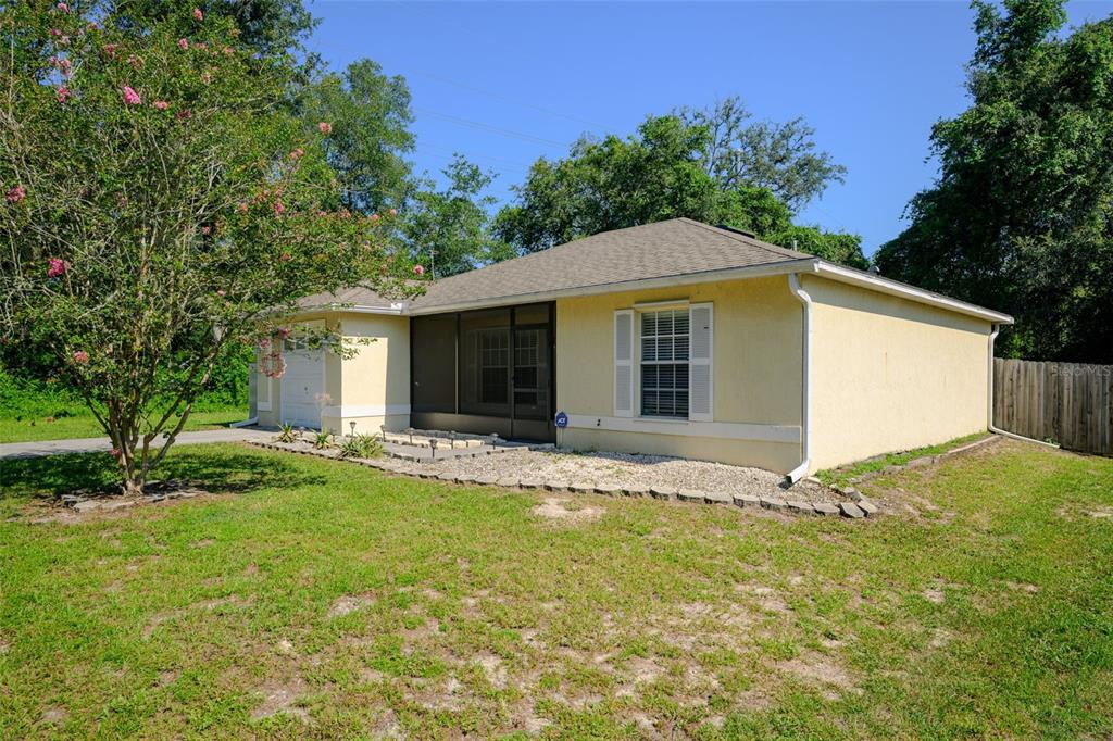 A yellow single-story house with a screened-in porch, a garage, and a gravel garden bed — 1491 16TH STREET, ORANGE CITY, FL