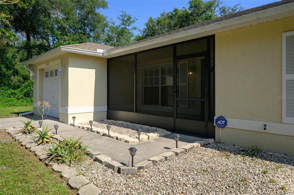 A yellow house exterior features a screened-in porch, a garage, and a gravel garden bed — 1491 16TH STREET, ORANGE CITY, FL