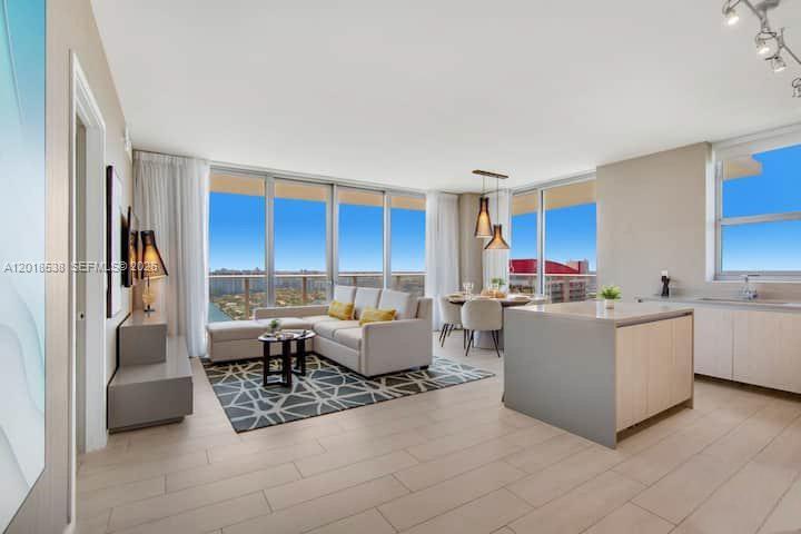 An open-concept living and dining area features floor-to-ceiling windows, light wood flooring, and modern furniture — 4010 S Ocean Dr # R2708, Hollywood FL 33019, HOLLYWOOD, FL