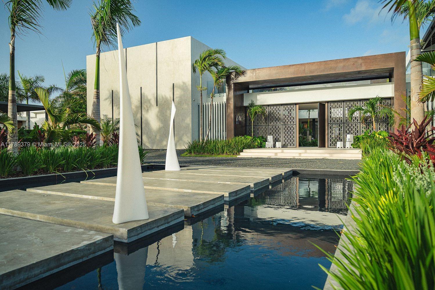A modern house exterior features a reflecting pool with concrete stepping stones and tall sculptures — 000 154 Cap Cana 23000, Dominican Republic, DR, DR