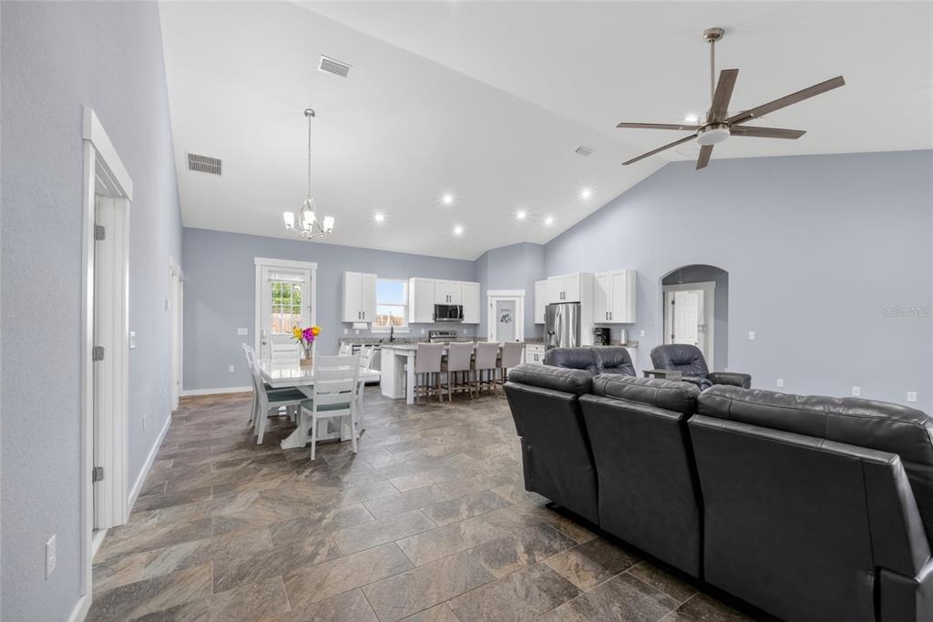 An open-concept kitchen and living area features vaulted ceilings, tile floors, and white cabinetry — 9449 SE 158TH PLACE, SUMMERFIELD, FL