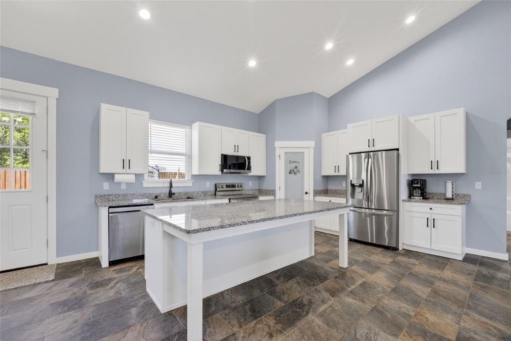A kitchen features white cabinets, granite countertops, a central island, and dark tile flooring — 9449 SE 158TH PLACE, SUMMERFIELD, FL