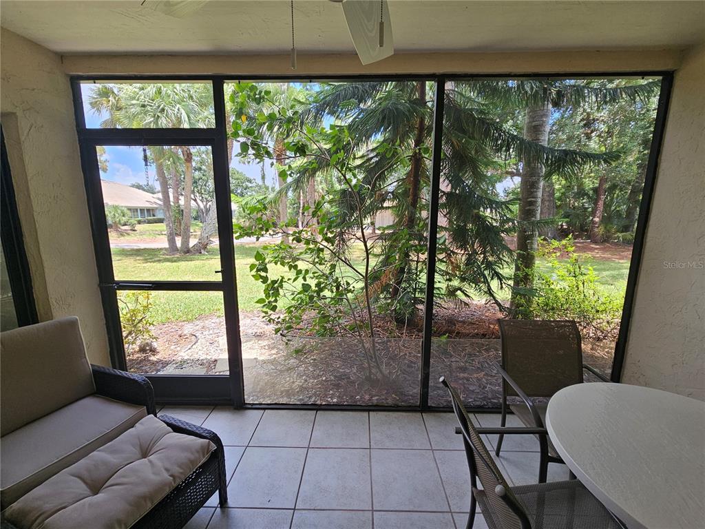 A screened-in patio with tile flooring, outdoor furniture, and a view of trees and grass — 5286 WILLOW LINKS UNIT 59, SARASOTA, FL