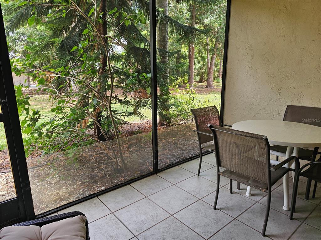 A screened-in patio features tiled flooring, a small round table, and chairs overlooking trees — 5286 WILLOW LINKS UNIT 59, SARASOTA, FL