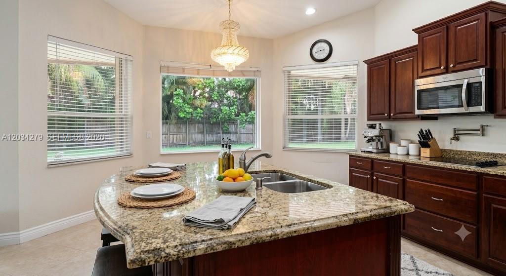 A kitchen features a granite-topped island, dark wood cabinets, and large windows overlooking a yard — 10255 Guatemala St, Cooper City FL 33026, COOPER CITY, FL