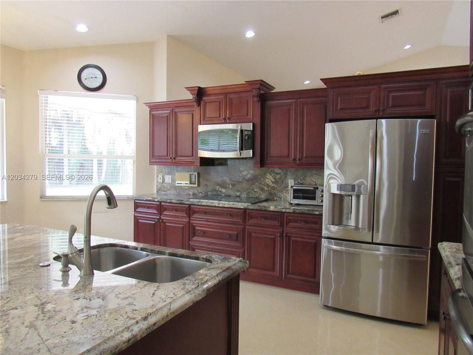 A kitchen features dark wood cabinets, granite countertops, stainless steel appliances, and a central island — 10255 Guatemala St, Cooper City FL 33026, COOPER CITY, FL