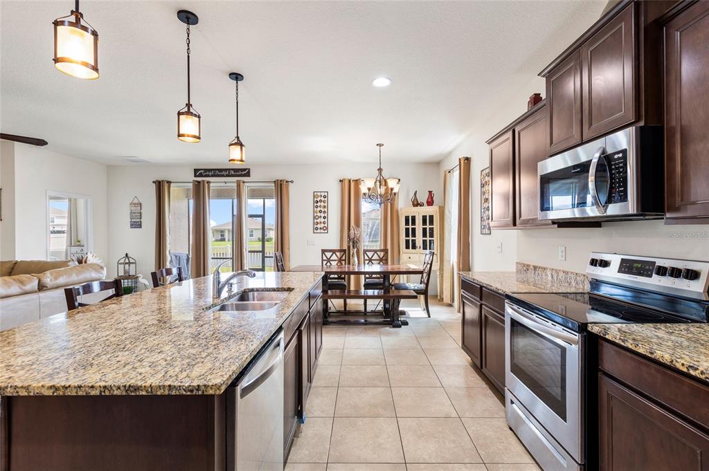 A kitchen with granite countertops, dark wood cabinets, and stainless steel appliances overlooks a dining area — 5025 JACKEL CHASE DRIVE, WIMAUMA, FL