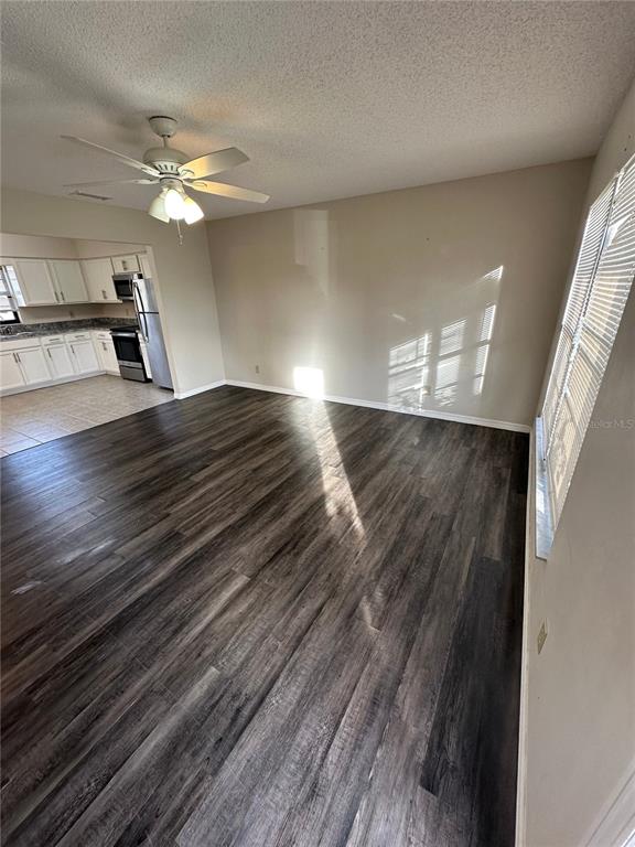 A living room with dark wood-look flooring, a ceiling fan, and an adjacent kitchen — 111 LOUISIANA AVENUE, ST CLOUD, FL
