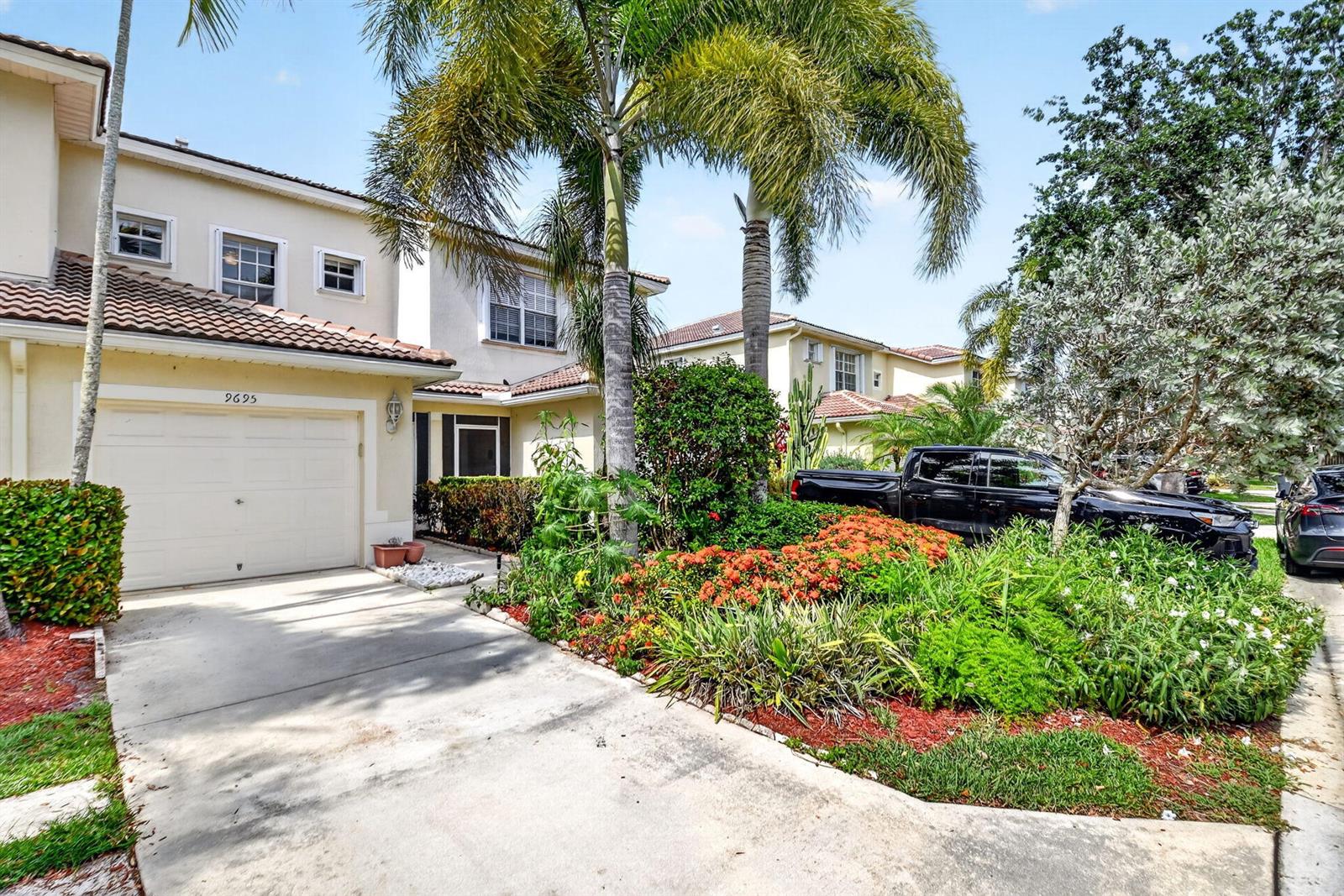 A two-story house with a garage, driveway, and lush landscaping under a bright sky — 9695 Porta Leona Lane, Boynton Beach FL 33472, BOYNTON BEACH, FL