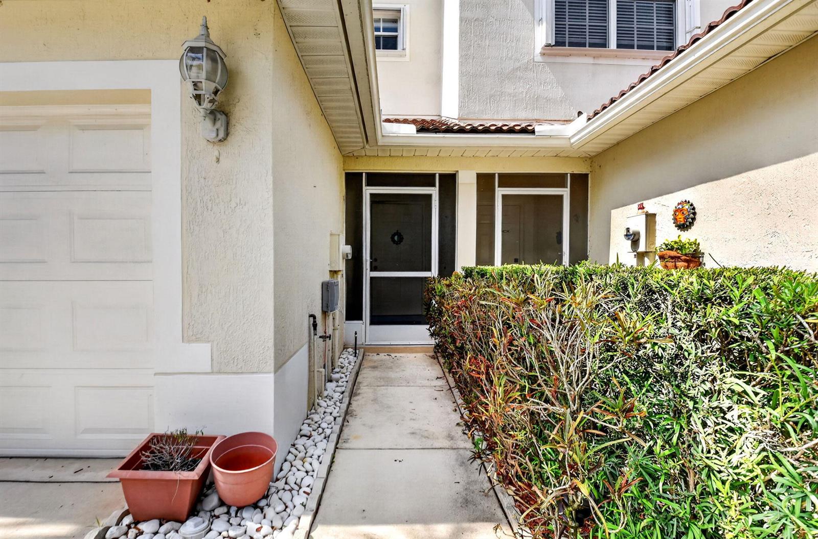 A concrete walkway leads to a front door with a screen door and a hedge — 9695 Porta Leona Lane, Boynton Beach FL 33472, BOYNTON BEACH, FL