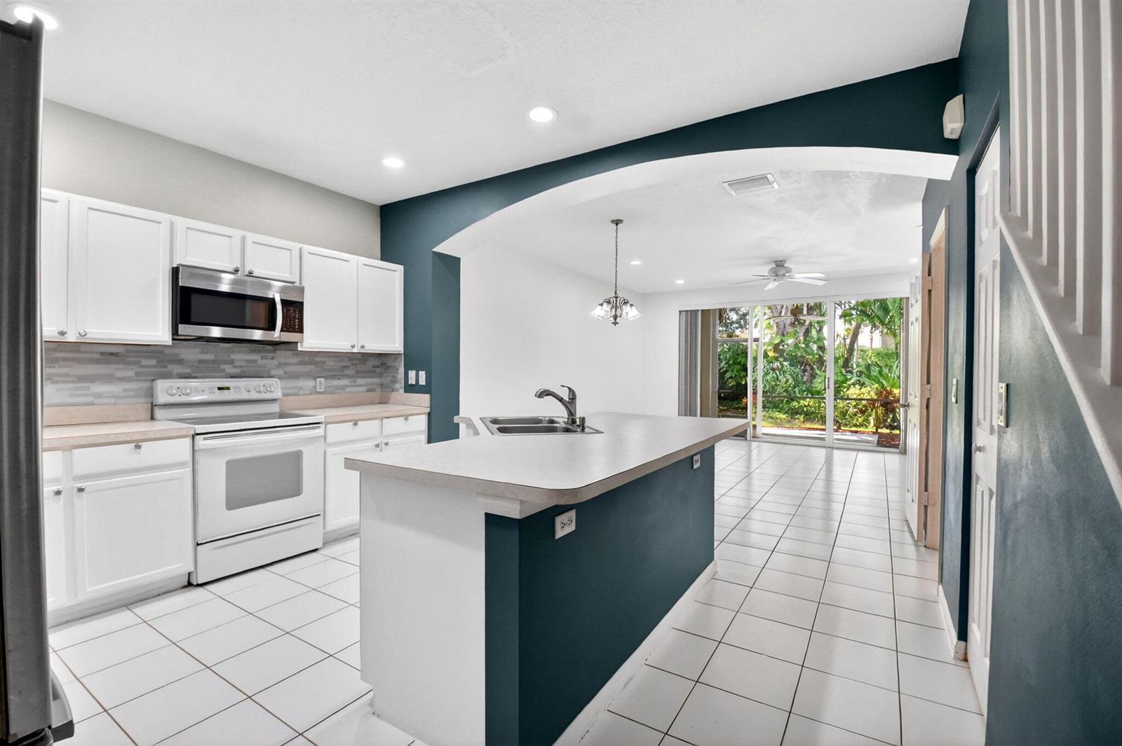 A kitchen with white cabinets, a central island, and tile flooring opens to a dining area — 9695 Porta Leona Lane, Boynton Beach FL 33472, BOYNTON BEACH, FL