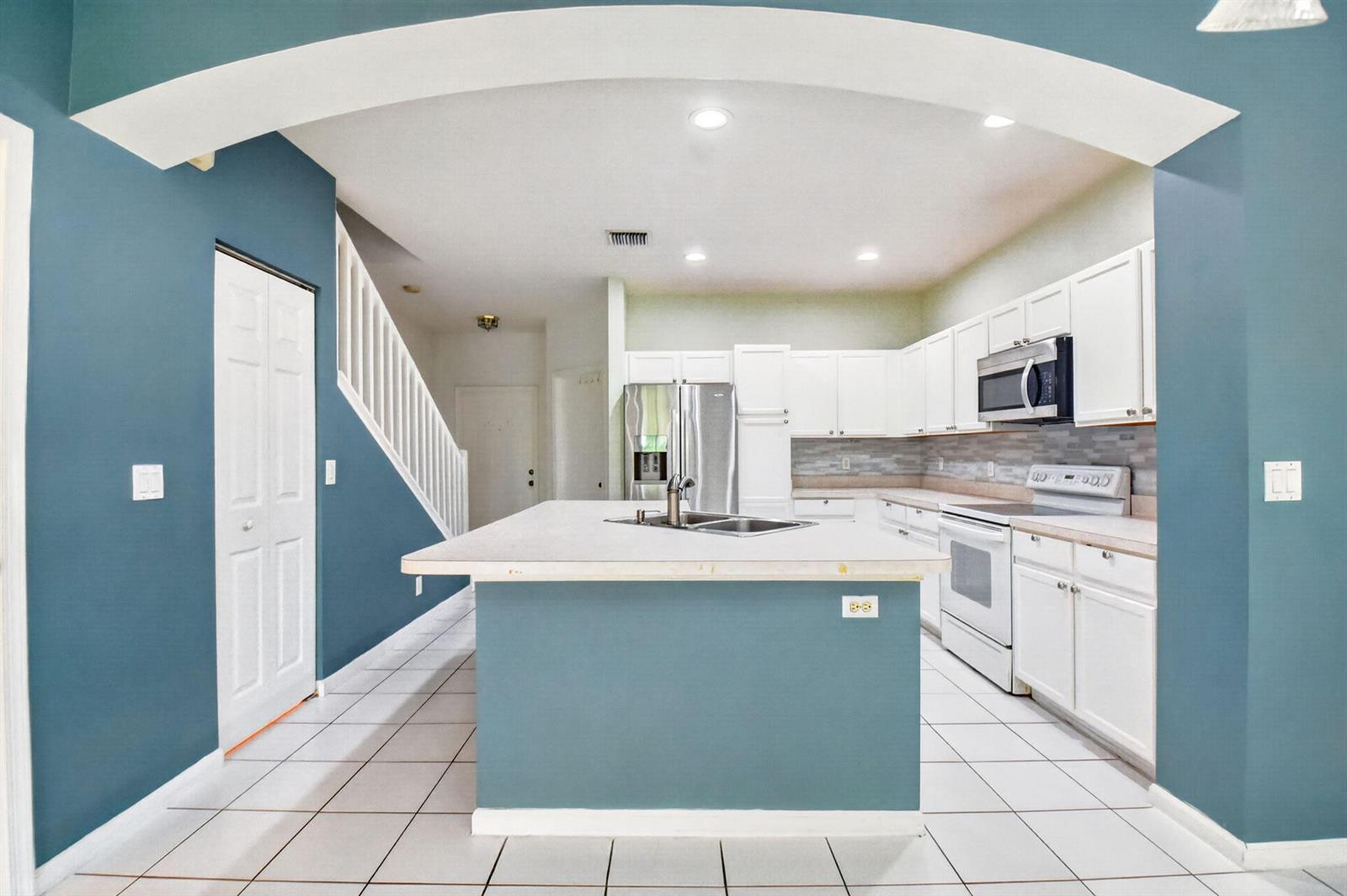 A kitchen features a blue island, white cabinets, stainless steel appliances, and white tile flooring — 9695 Porta Leona Lane, Boynton Beach FL 33472, BOYNTON BEACH, FL