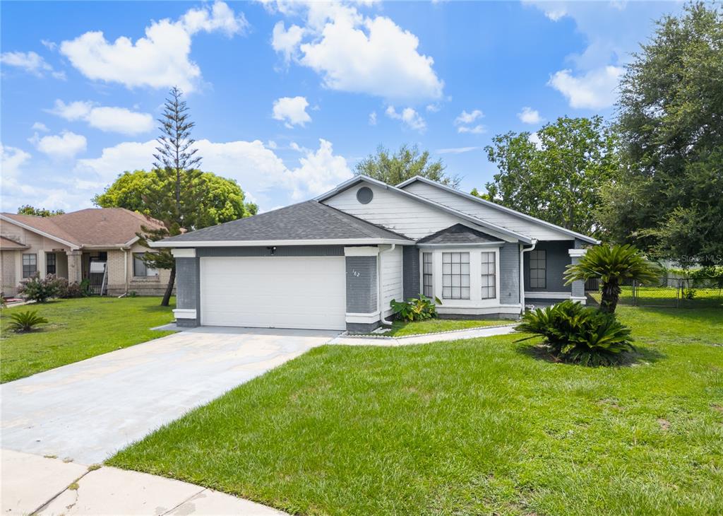 A single-story house with a white garage, gray brick accents, and a front lawn — 182 PINEWOOD CIRCLE, KISSIMMEE, FL