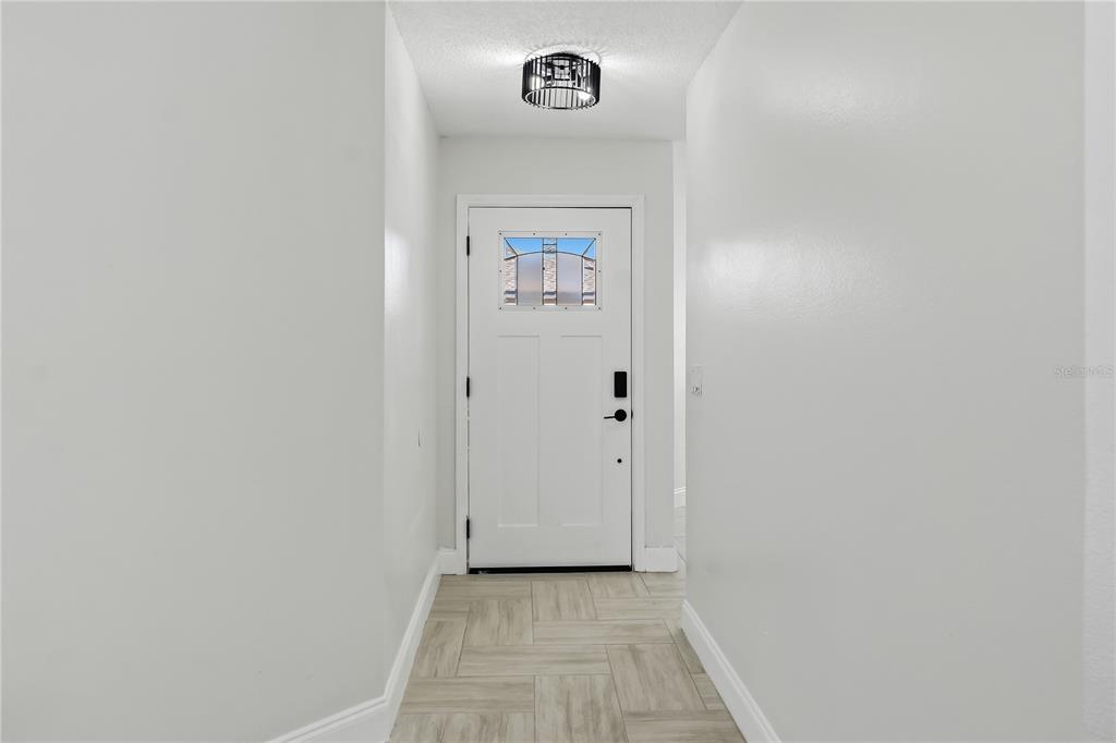 A white front door with a glass insert sits at the end of a hallway — 182 PINEWOOD CIRCLE, KISSIMMEE, FL