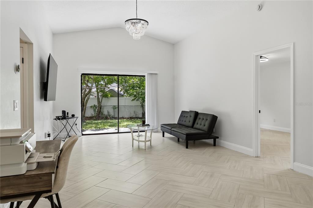 A bright living room features white walls, herringbone tile flooring, a chandelier, and sliding glass doors — 182 PINEWOOD CIRCLE, KISSIMMEE, FL