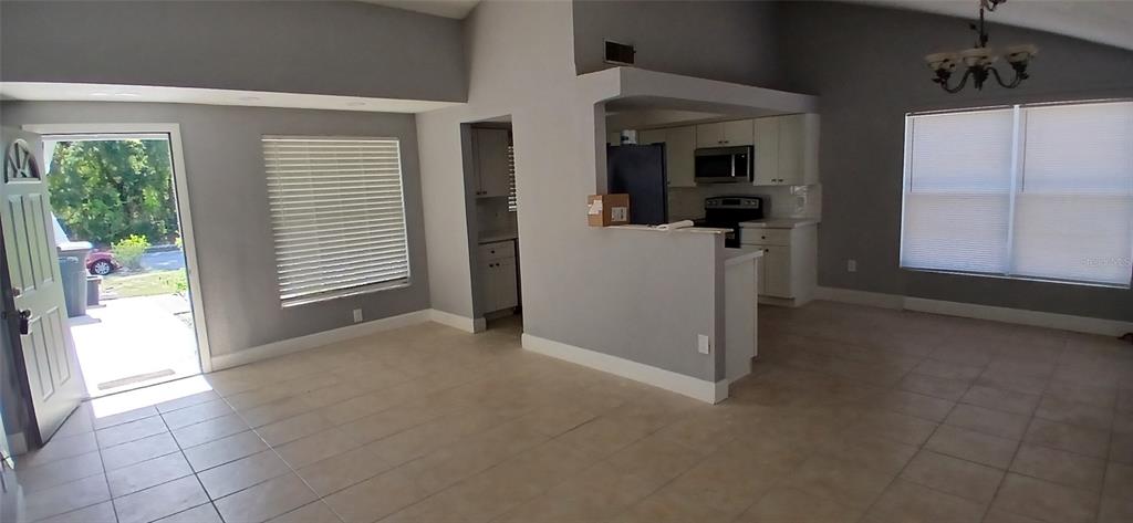 An open-concept living and dining area features tile flooring, gray walls, and a kitchen pass-through — 1019 PENINSULA ROAD, TARPON SPRINGS, FL