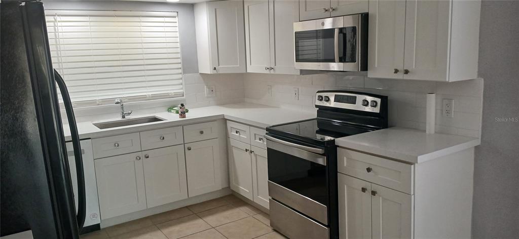 A kitchen features white cabinets, stainless steel appliances, a white subway tile backsplash, and countertops — 1019 PENINSULA ROAD, TARPON SPRINGS, FL