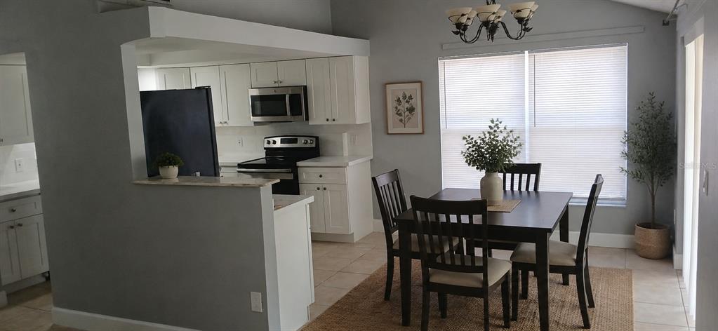 A kitchen with white cabinets and a dining area with a table and chairs — 1019 PENINSULA ROAD, TARPON SPRINGS, FL