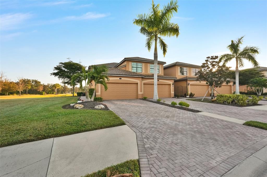 A two-story house with a tan stucco exterior, tile roof, and a paved driveway — 6911 GRAND ESTUARY TRAIL UNIT 102, BRADENTON, FL