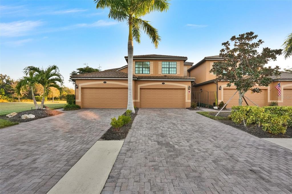 A two-story townhouse with a paved driveway, two garage doors, and a palm tree — 6911 GRAND ESTUARY TRAIL UNIT 102, BRADENTON, FL