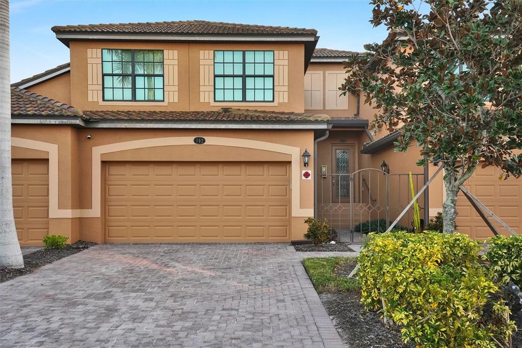 A two-story tan stucco house features a two-car garage and a paved driveway — 6911 GRAND ESTUARY TRAIL UNIT 102, BRADENTON, FL