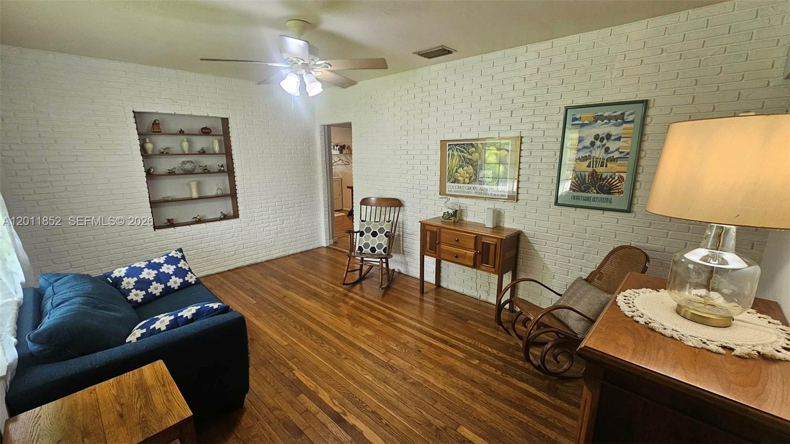 A living room features white brick walls, hardwood floors, a blue sofa, and rocking chairs — 831 Wren Ave, Miami Springs FL 33166, MIAMI SPRINGS, FL