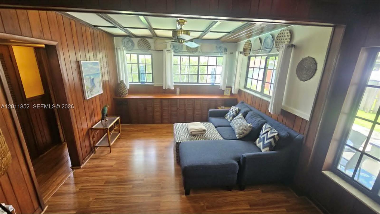 A living room features wood-paneled walls, a blue sectional sofa, and multiple windows — 831 Wren Ave, Miami Springs FL 33166, MIAMI SPRINGS, FL