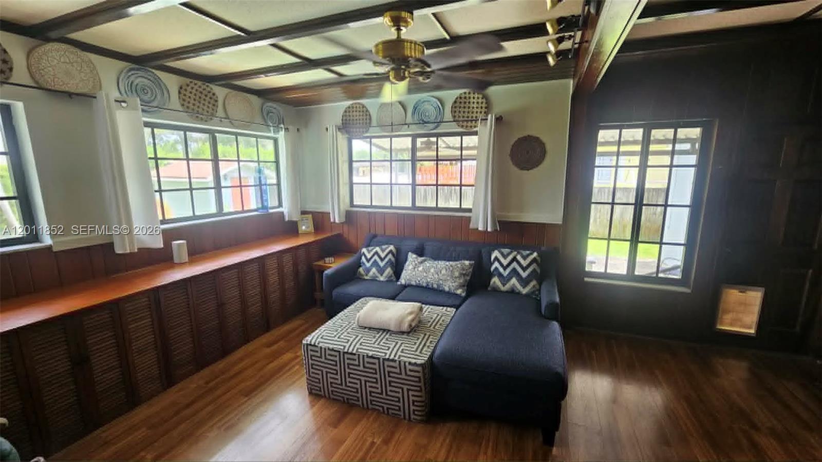 A living room features a blue sectional sofa, wood paneling, and a coffered ceiling — 831 Wren Ave, Miami Springs FL 33166, MIAMI SPRINGS, FL