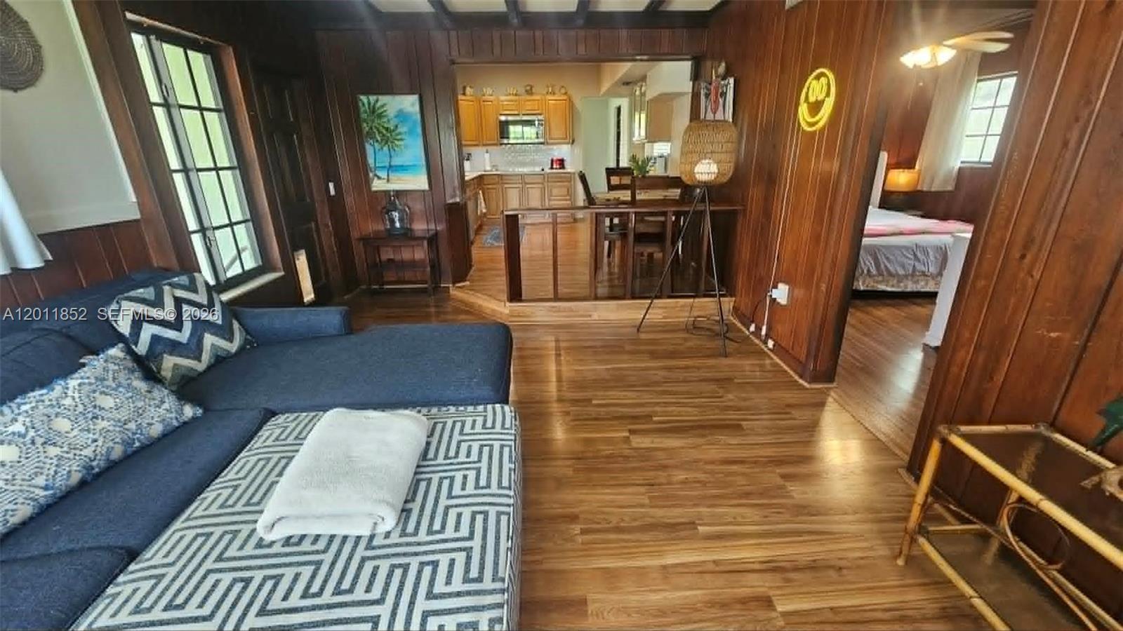 A living room with wood-paneled walls leads to a kitchen and a bedroom — 831 Wren Ave, Miami Springs FL 33166, MIAMI SPRINGS, FL