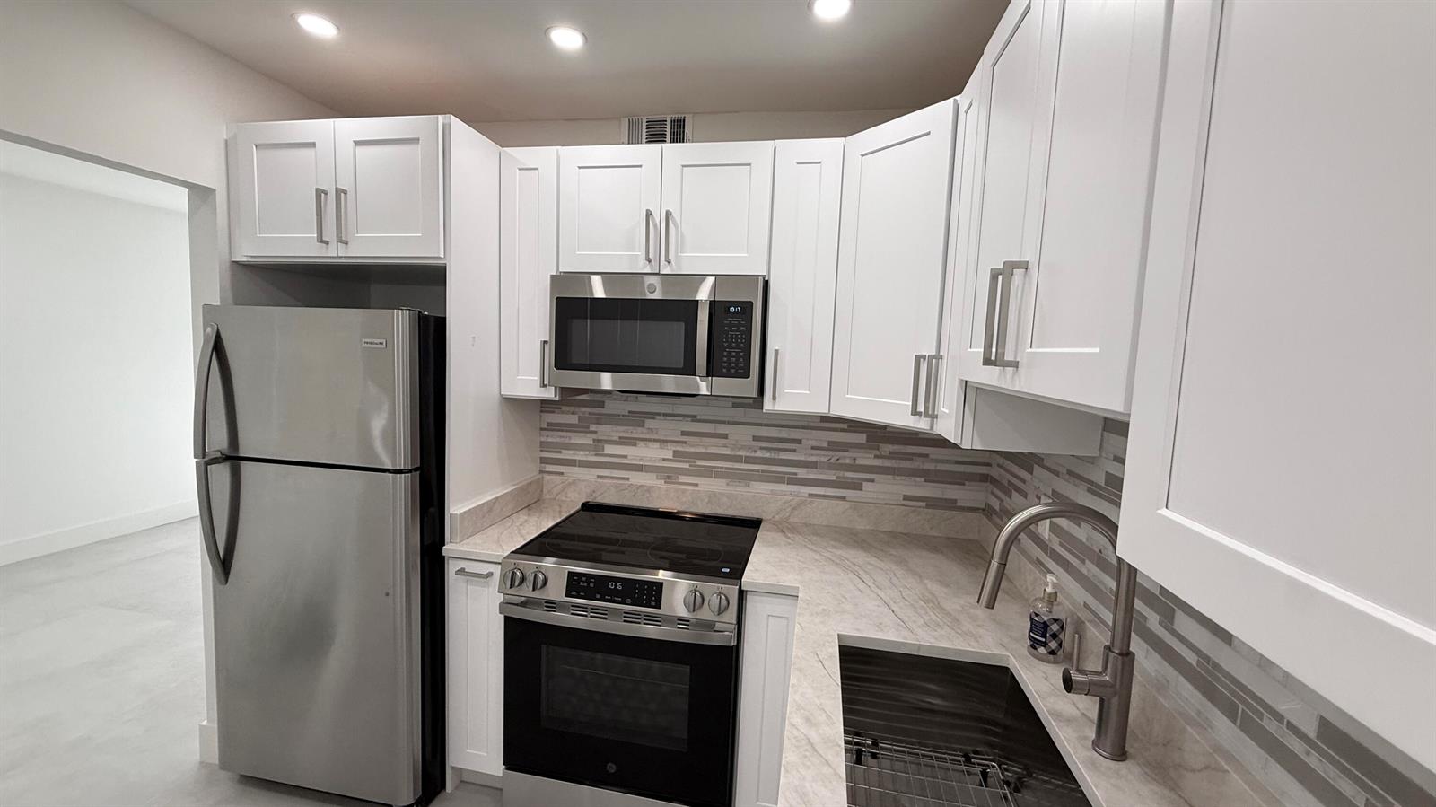 A kitchen features white cabinets, stainless steel appliances, a tiled backsplash, and stone countertops — 6505 Winfield Boulevard, Margate FL 33063, MARGATE, FL