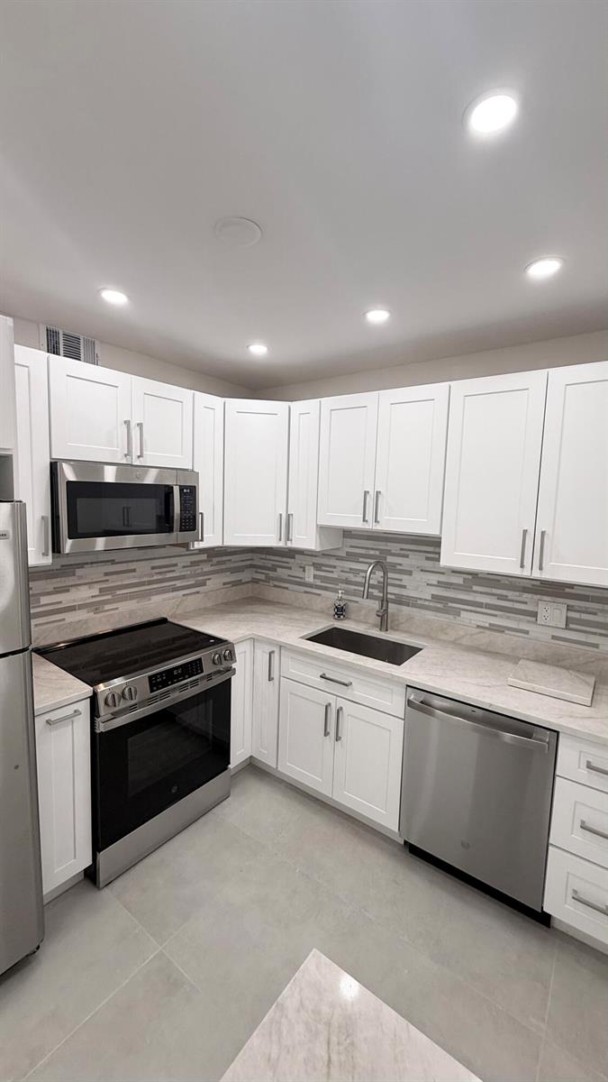 A kitchen features white cabinets, stainless steel appliances, a tiled backsplash, and light-colored countertops — 6505 Winfield Boulevard, Margate FL 33063, MARGATE, FL