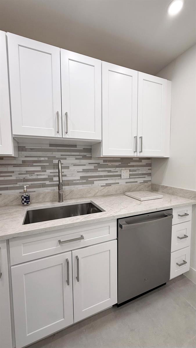 A kitchen features white cabinets, a stainless steel sink, a dishwasher, and a tiled backsplash — 6505 Winfield Boulevard, Margate FL 33063, MARGATE, FL