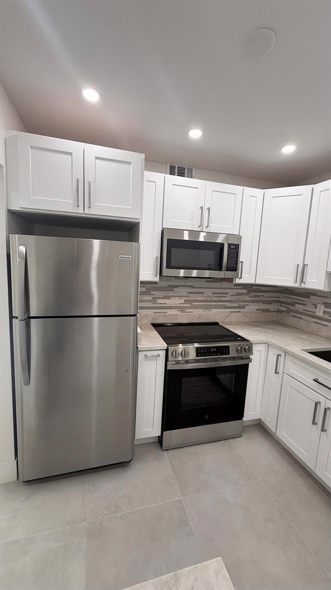 A kitchen features white cabinets, stainless steel appliances, and a gray tiled backsplash — 6505 Winfield Boulevard, Margate FL 33063, MARGATE, FL