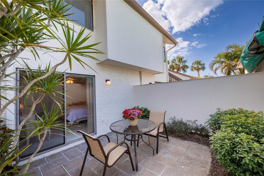 A small stone patio features a glass-topped table, two chairs, and a sliding glass door — 696 BIRD BAY DRIVE W UNIT 138, VENICE, FL
